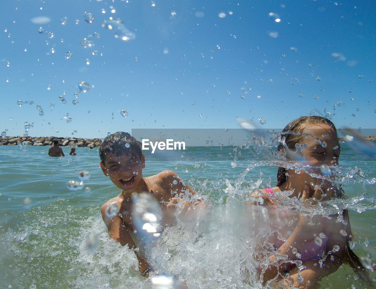 Playful siblings having fun in sea against sky during sunny day