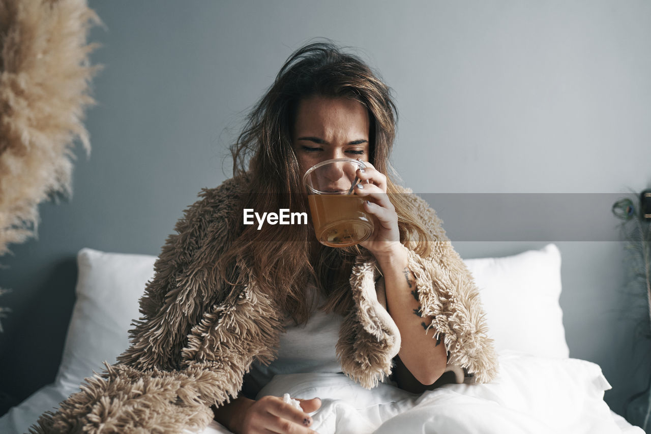 Close-up of woman drinking lemon tea sitting on bed