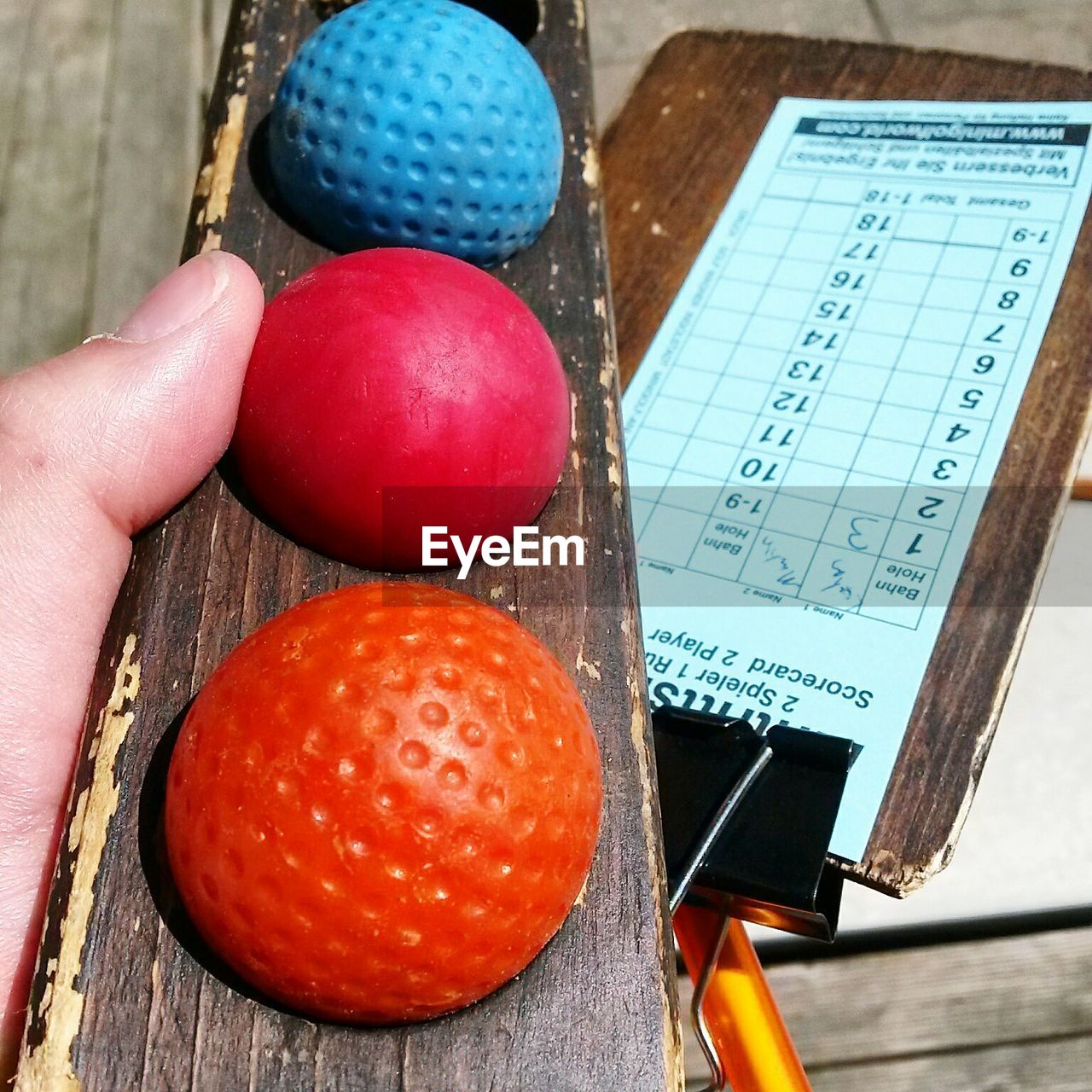 Cropped hand of person holding miniature golf balls on wood