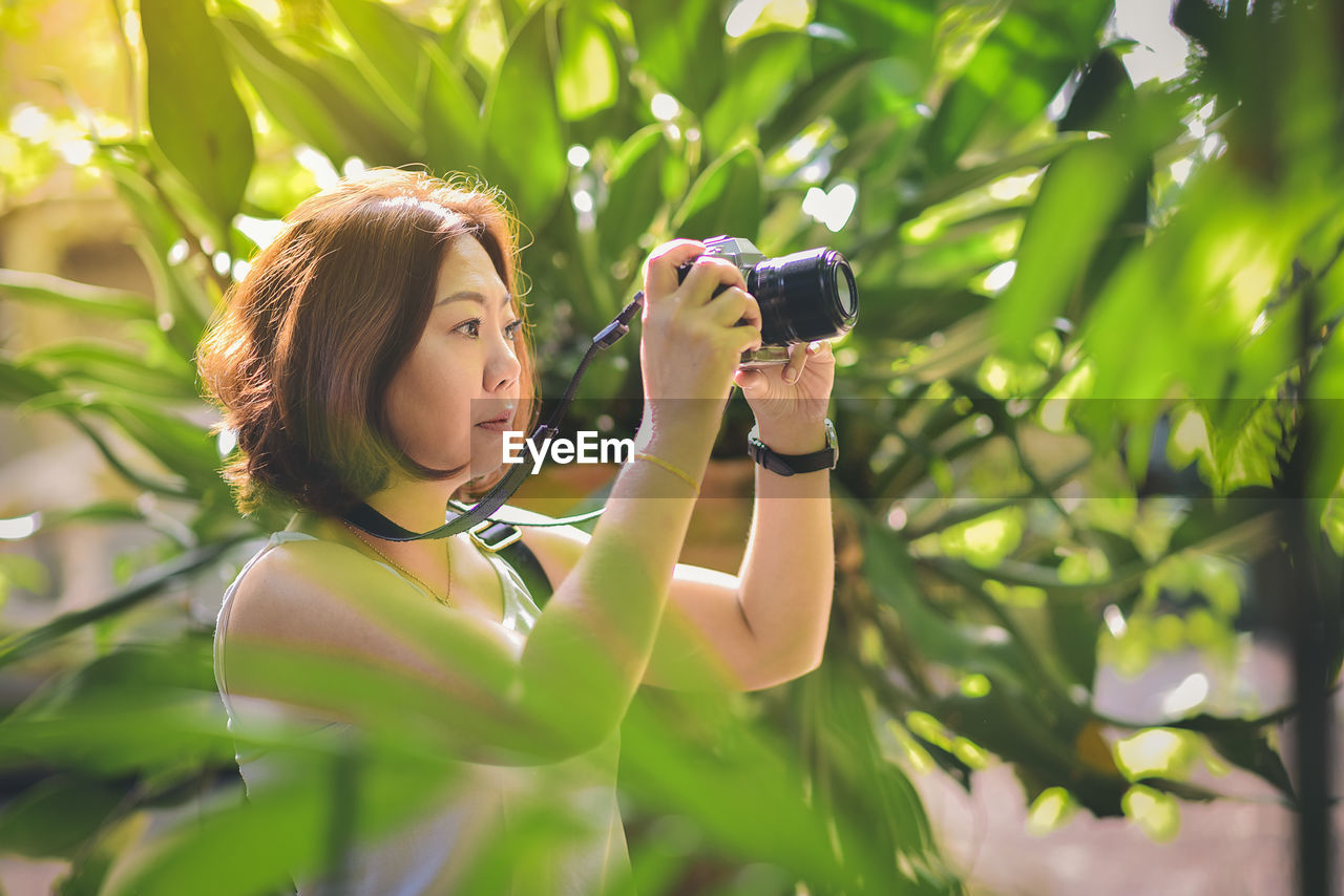 Mature woman photographing with camera while standing amidst plants