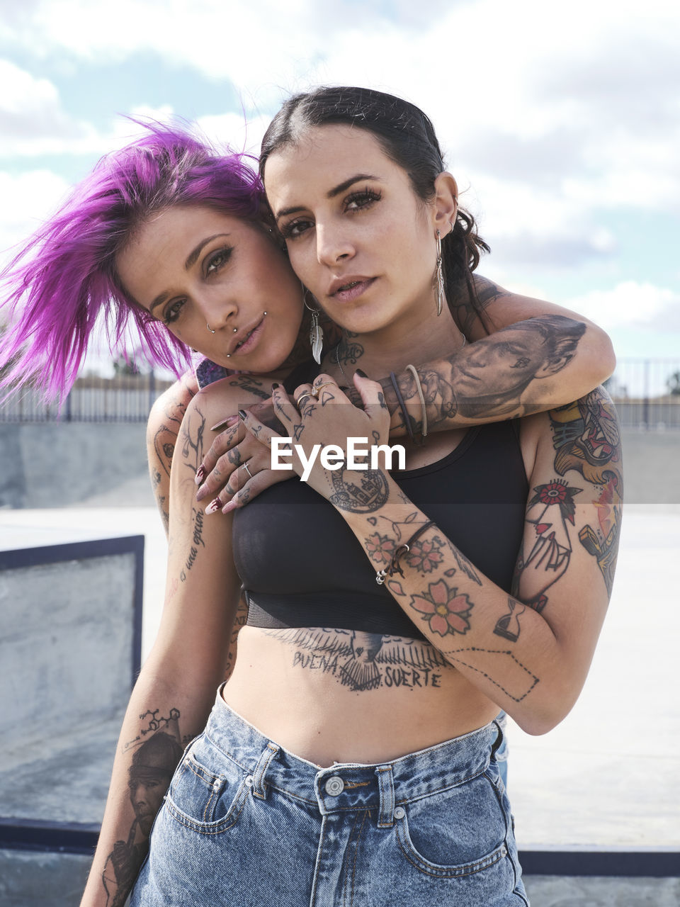 Female friends with eccentric appearance and tattoos embracing on street and looking at camera