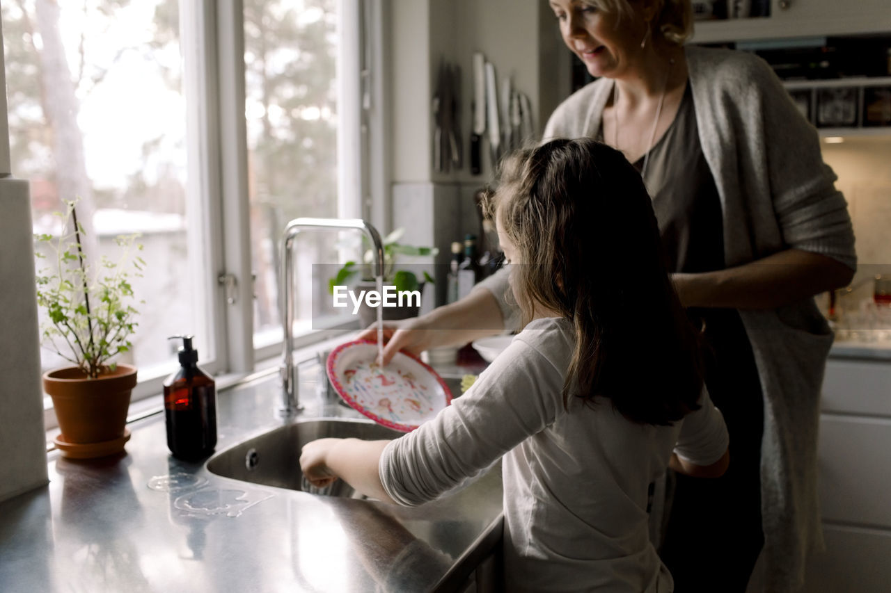 Daughter helping mother in kitchen at home