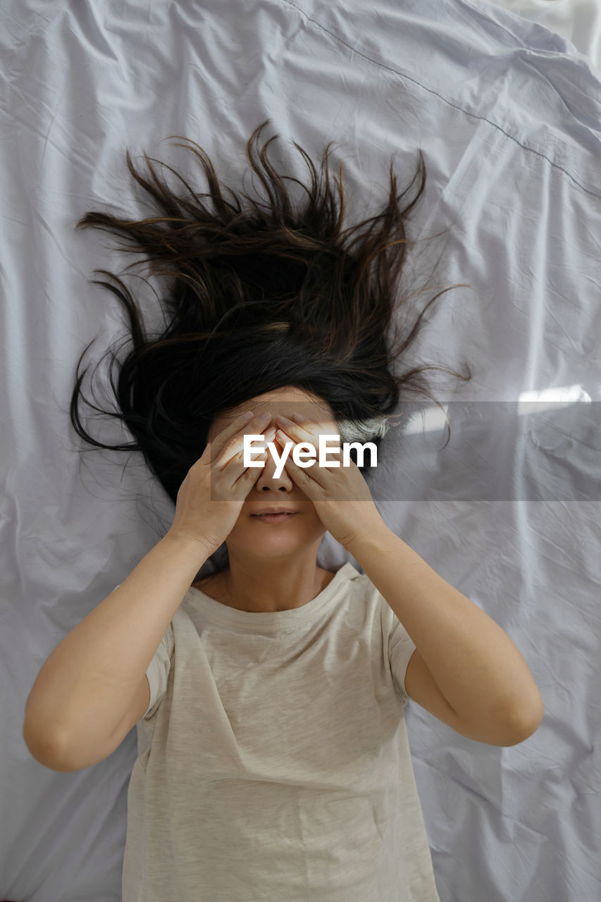 Portrait of young asian woman lying on bed at home on sunny day