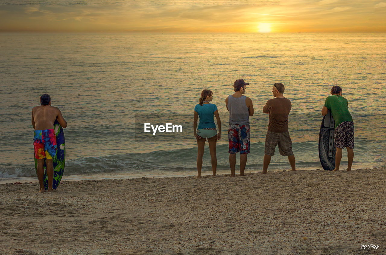 Rear view of people at beach during sunset