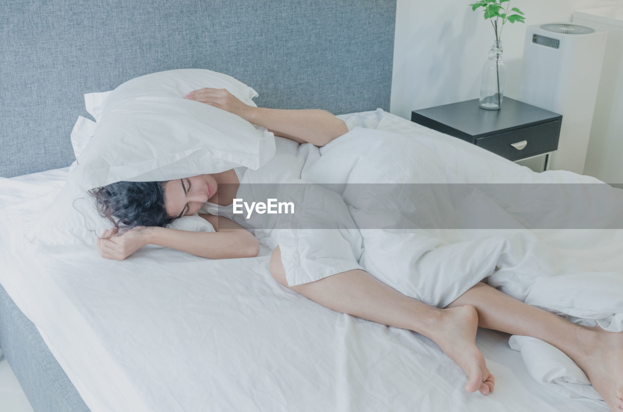 Woman covering ears with pillows while sleeping on bed