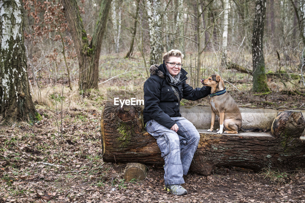 FULL LENGTH PORTRAIT OF MAN WITH DOG STANDING IN FOREST DURING AUTUMN