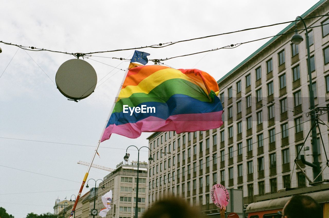 Rainbow flag waving in city against sky