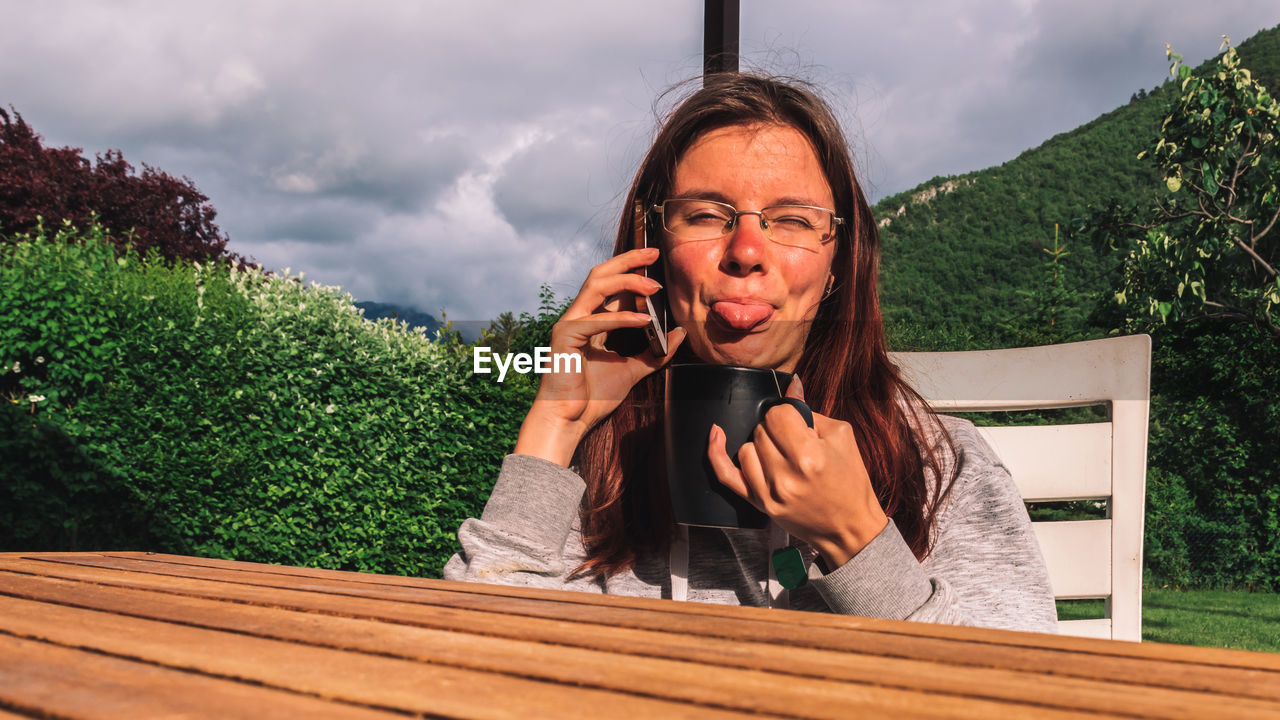 Portrait of woman talking on phone while making face sitting outdoors