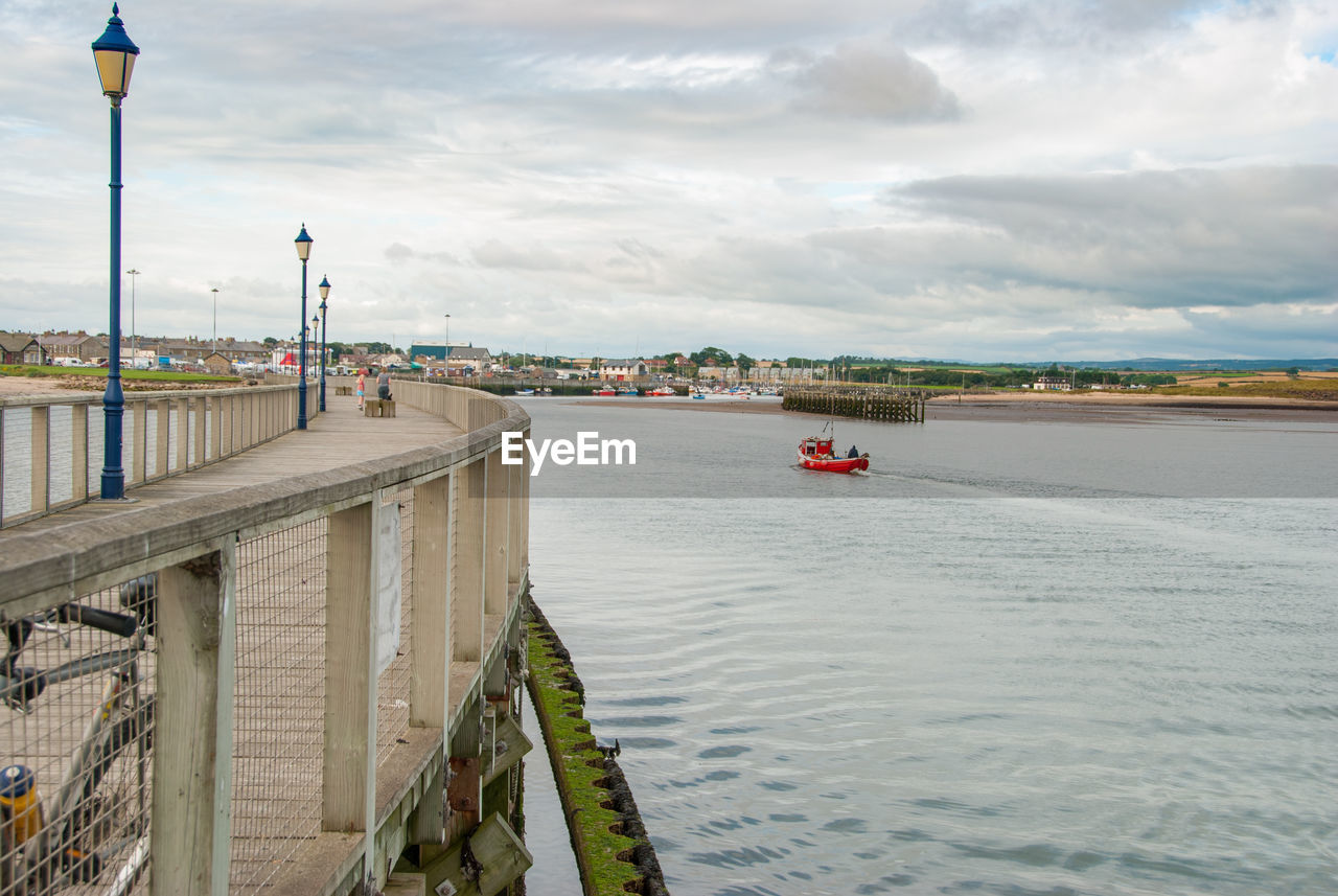 A small red fishing boat passes a pier on a calm day.