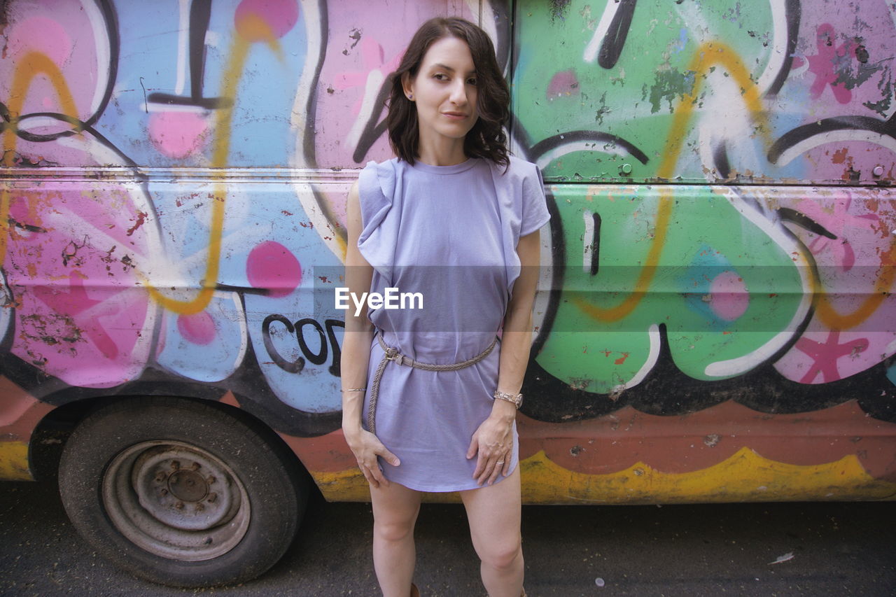 Young woman standing against graffiti on vehicle