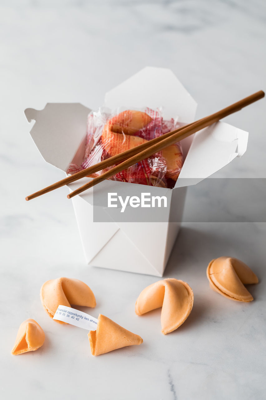 A takeout food container filled with fortune cookies with cookies in front.