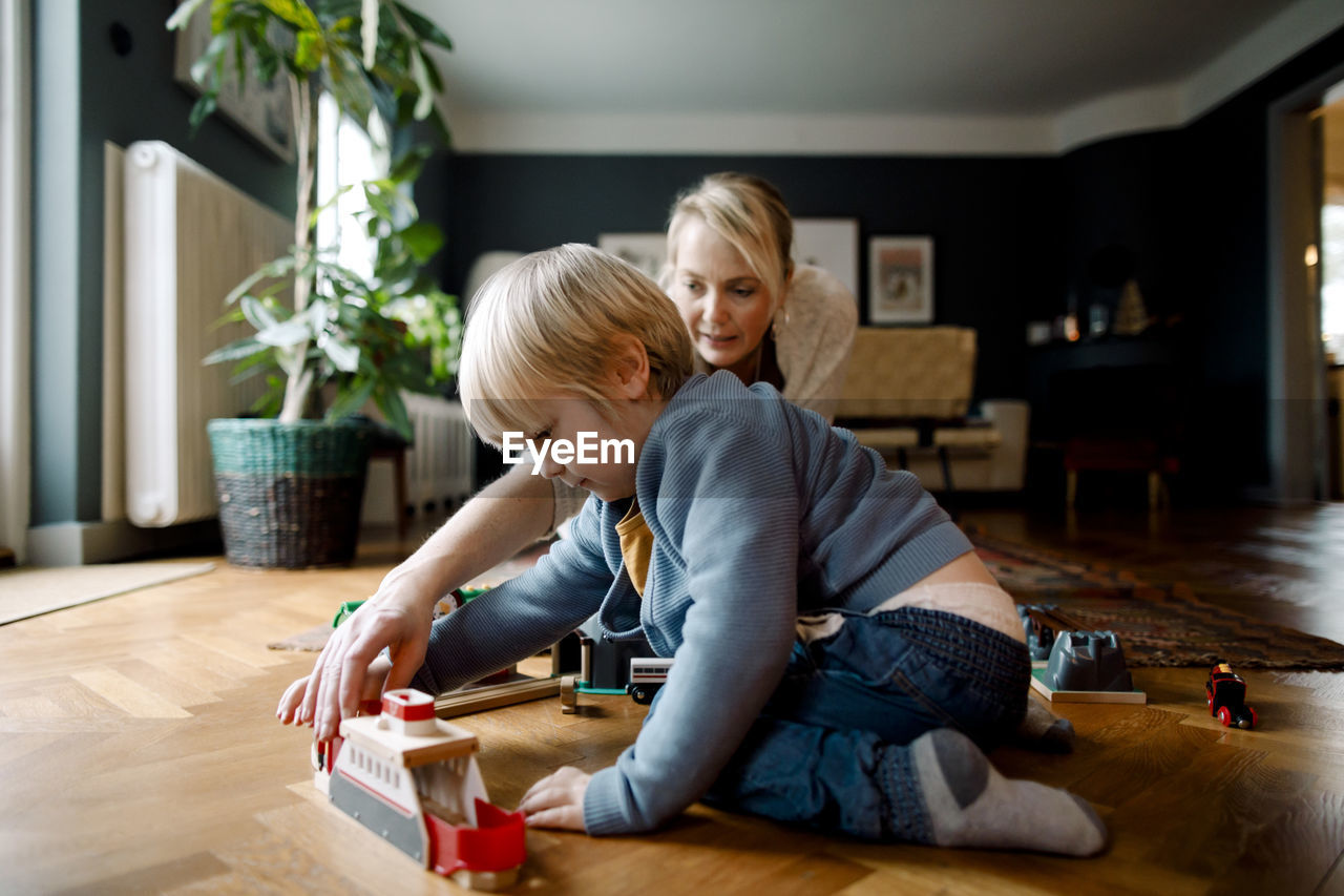 Mother and daughter playing with toy train on hardwood floor in living room at home