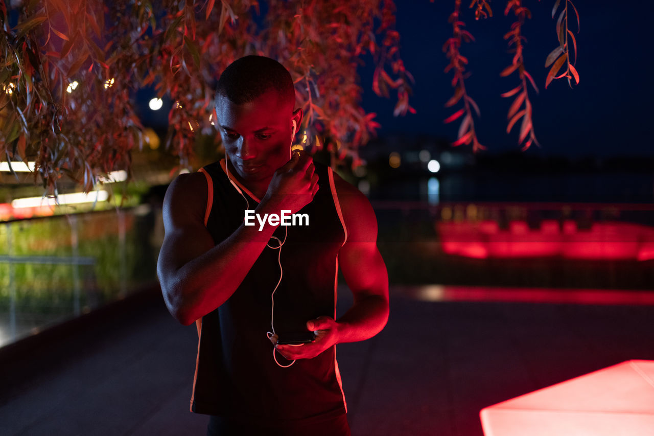 Ethnic athlete putting on earphones at night