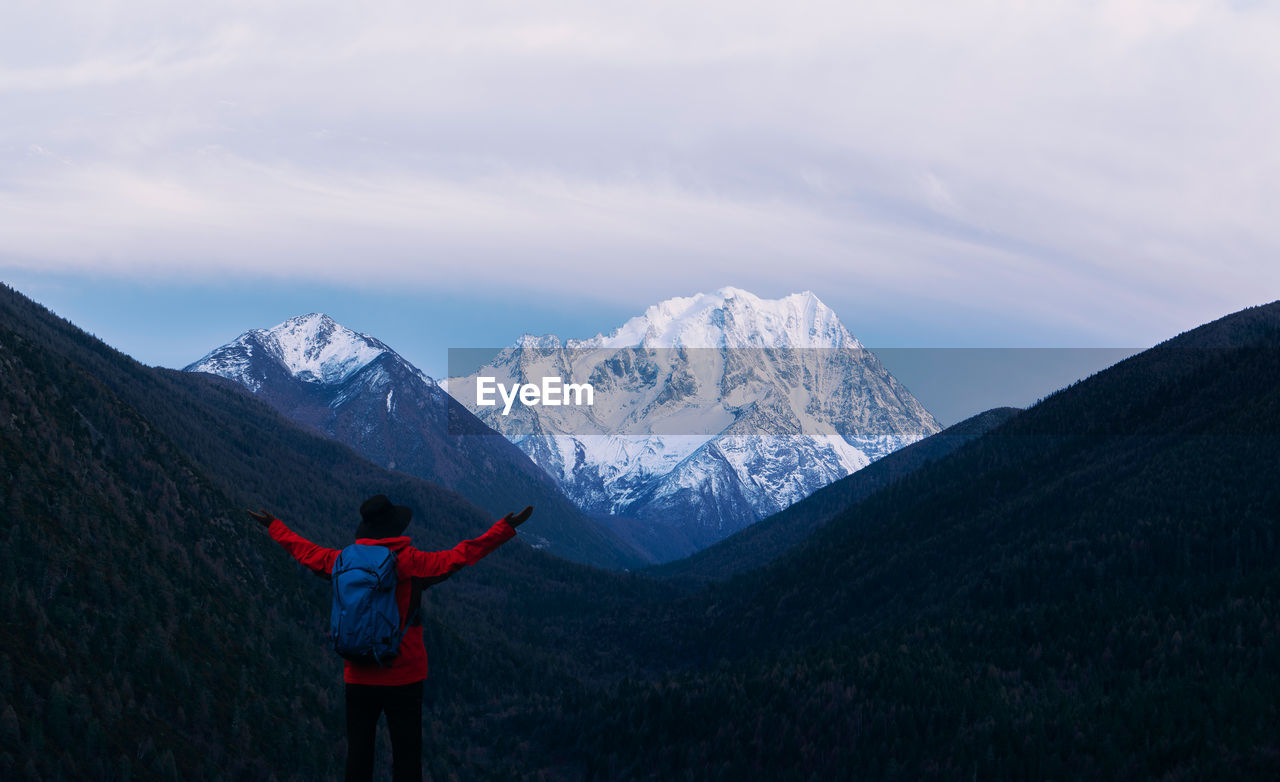 Rear view of hiker standing on mountain against sky