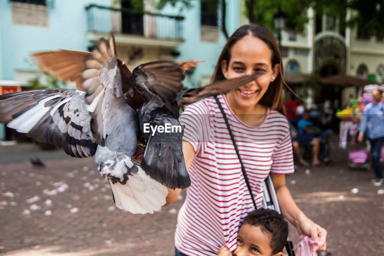 Smiling mother playing with pigeons by son in city