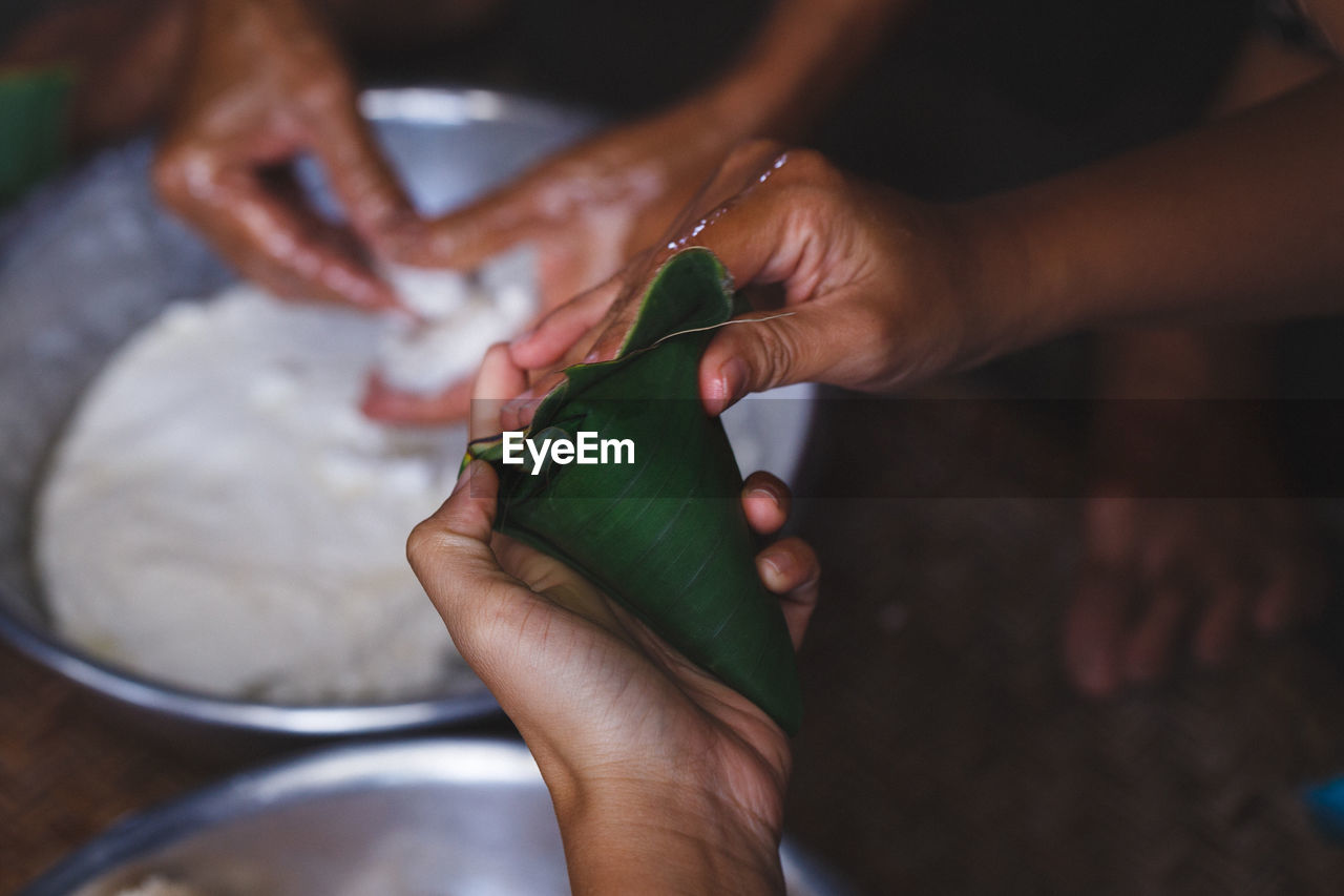 High angle view of woman wrapping rice cakes in banana leaf cone