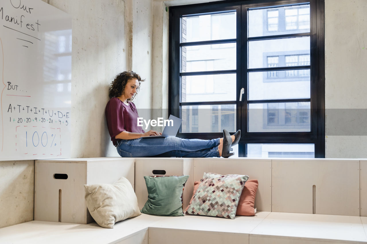 Female entrepreneur using laptop while sitting with legs crossed at ankle in office