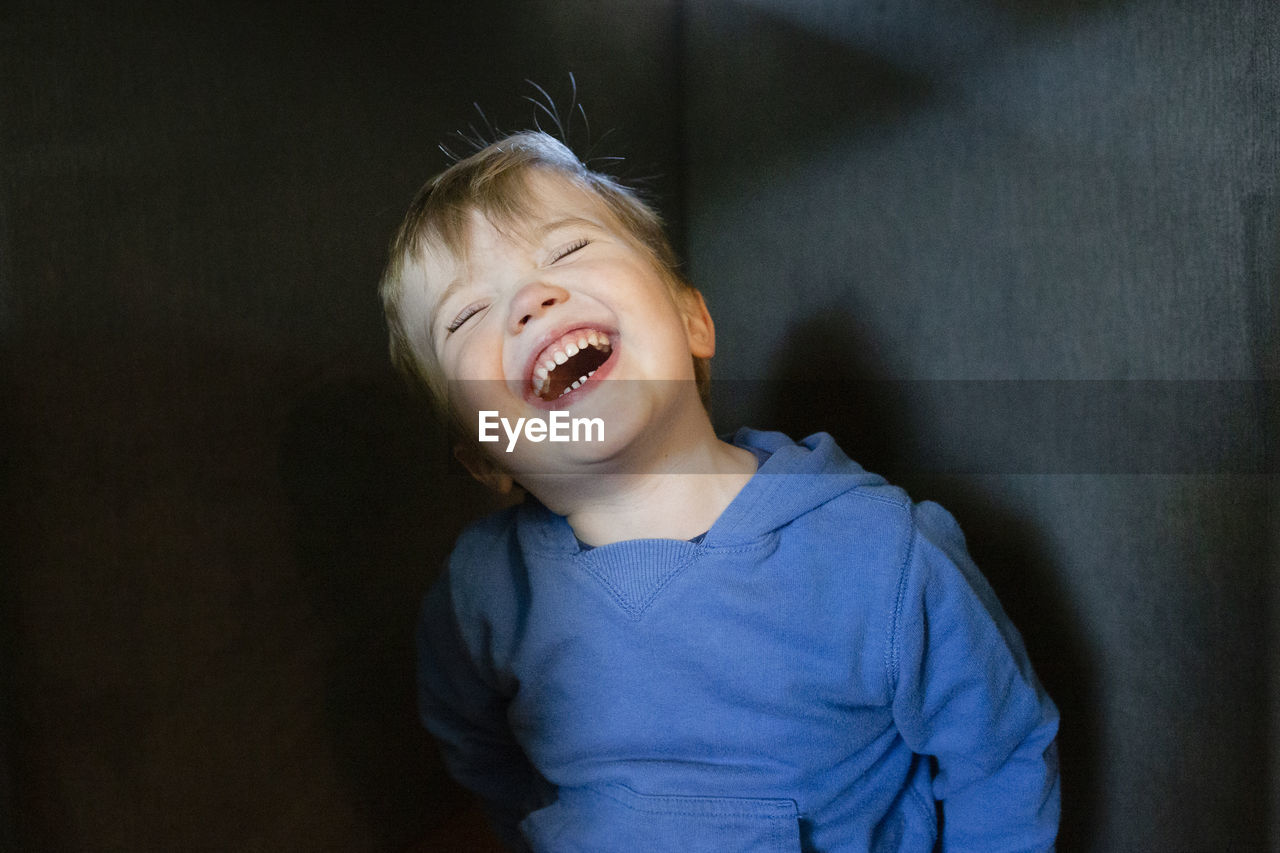 Joyful and happy toddler boy tilts head back while laughing indoors