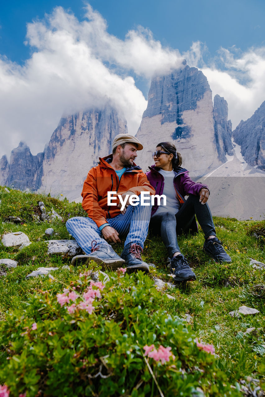 REAR VIEW OF PEOPLE SITTING ON MOUNTAIN