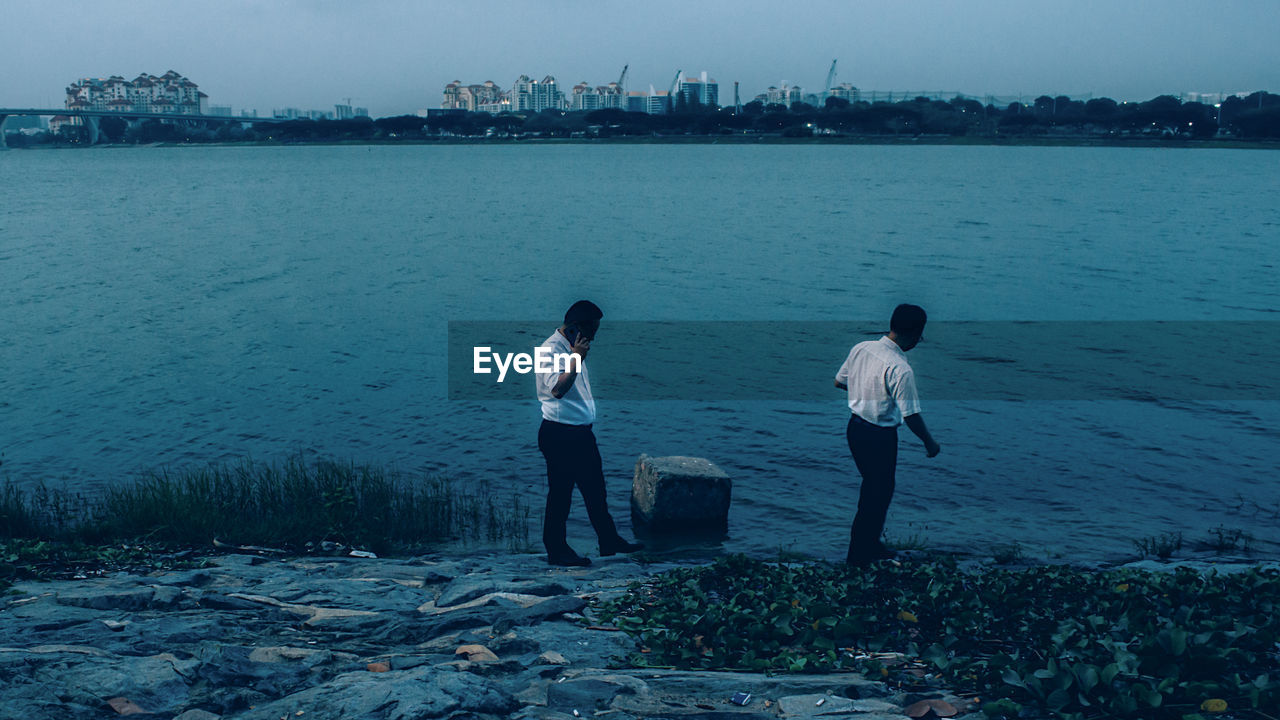 REAR VIEW OF PEOPLE STANDING ON SHORE AGAINST SEA