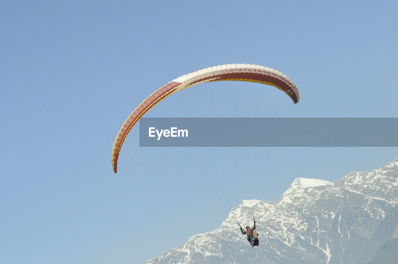 LOW ANGLE VIEW OF PERSON PARAGLIDING AGAINST CLEAR SKY DURING WINTER