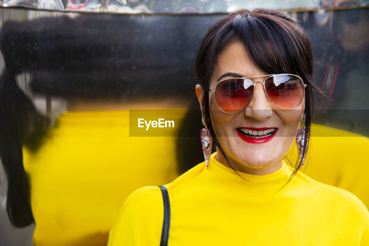 Fashionable mature woman wearing yellow top and sunglasses in city