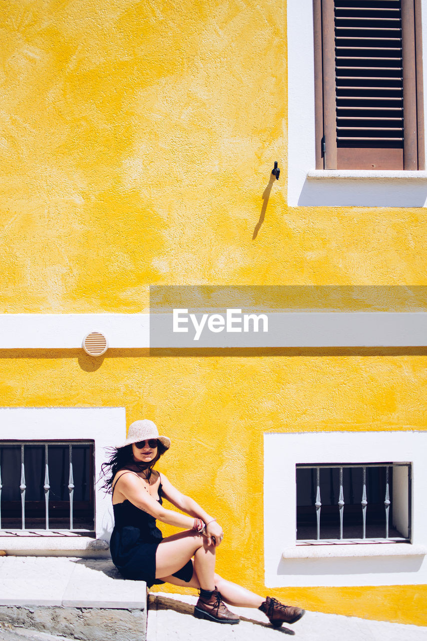 Young woman sitting against yellow building during sunny day