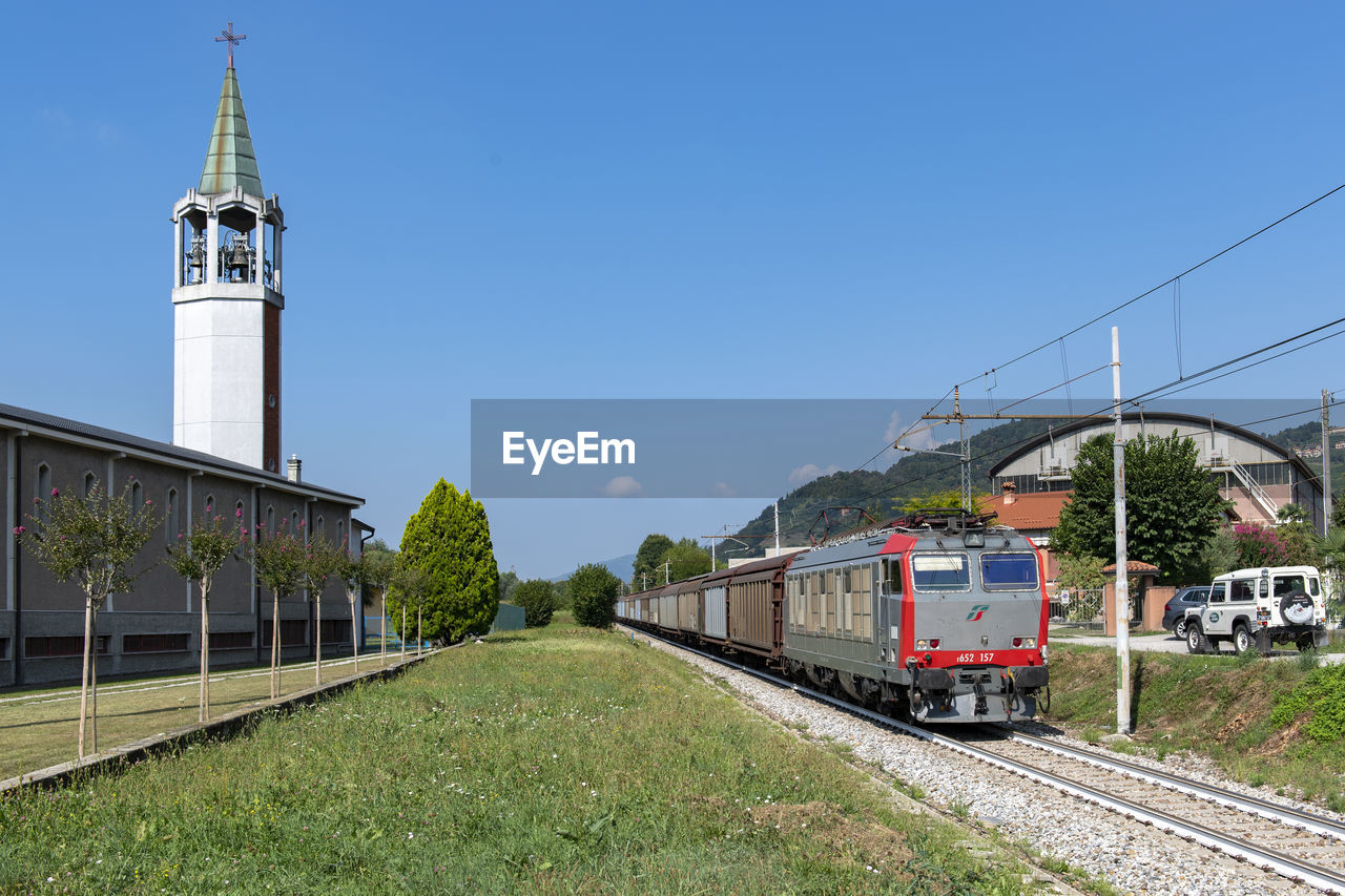 TRAIN ON RAILROAD TRACKS BY BUILDING AGAINST SKY