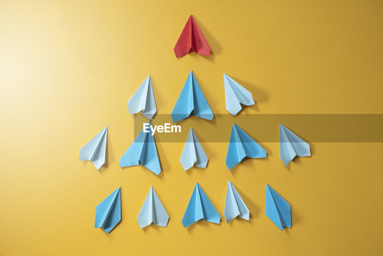 Blue paper aeroplane origami following rhe red one on yellow background