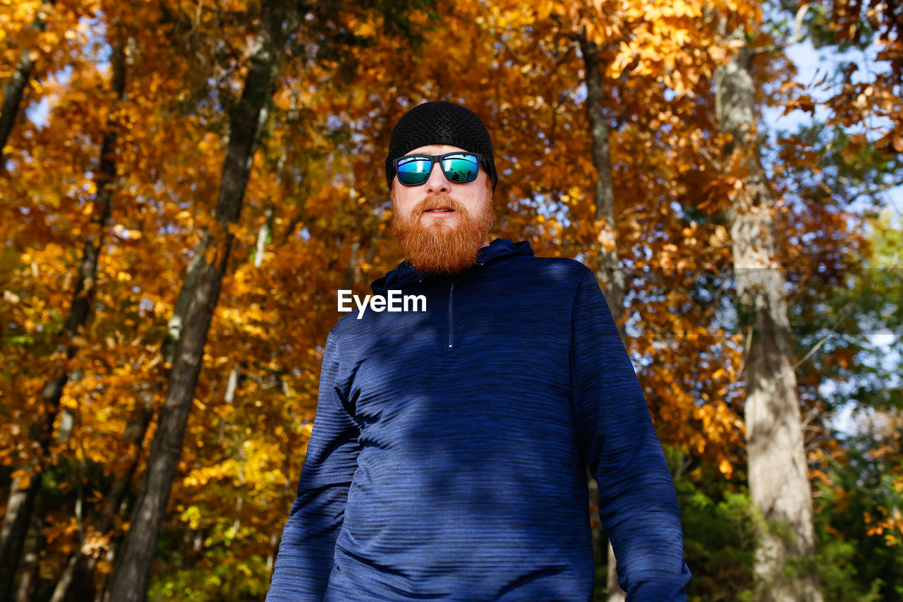 Portrait of bearded man in sunglasses standing against trees during autumn