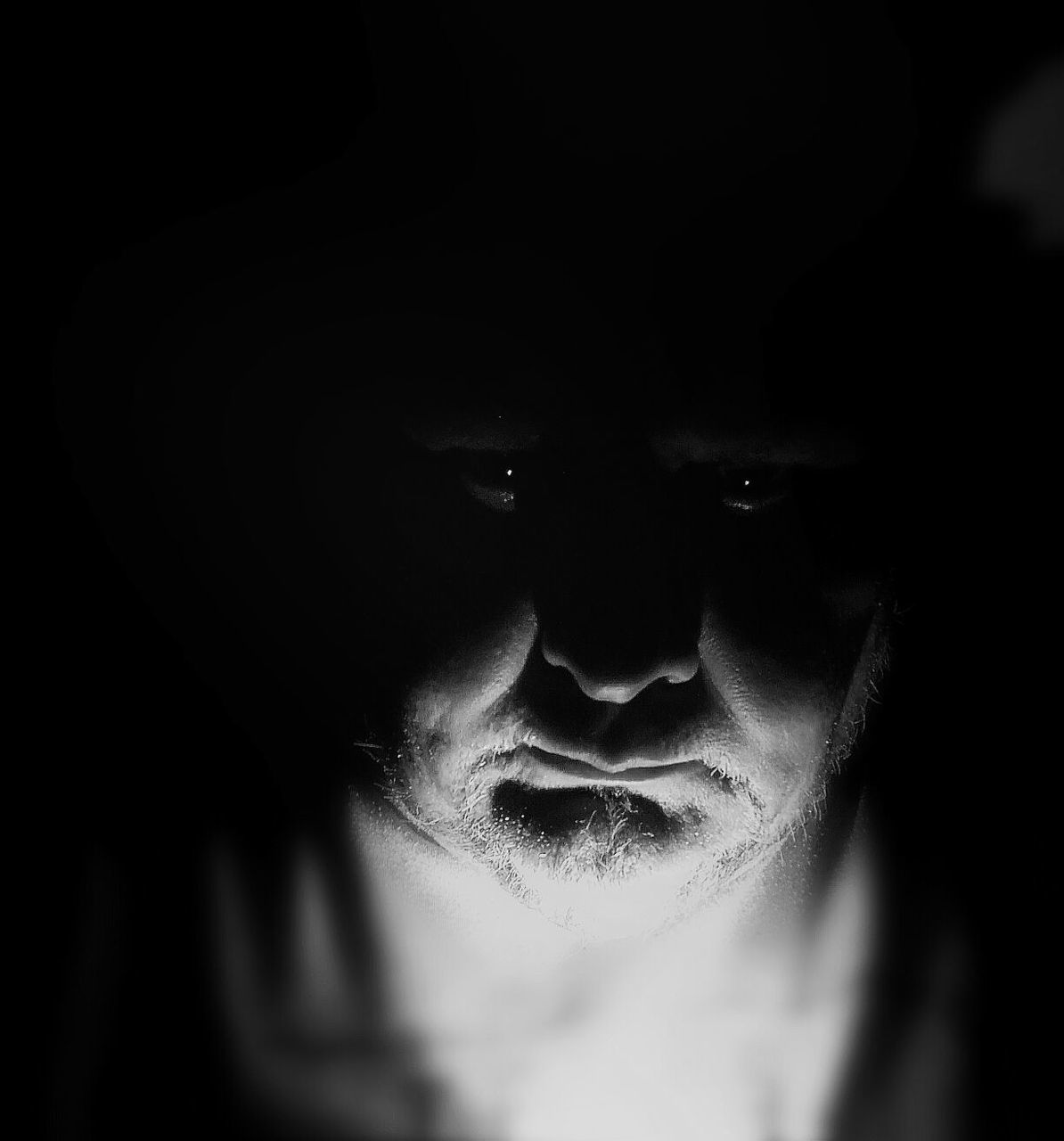 Close-up portrait of bearded man with light on his face in darkroom