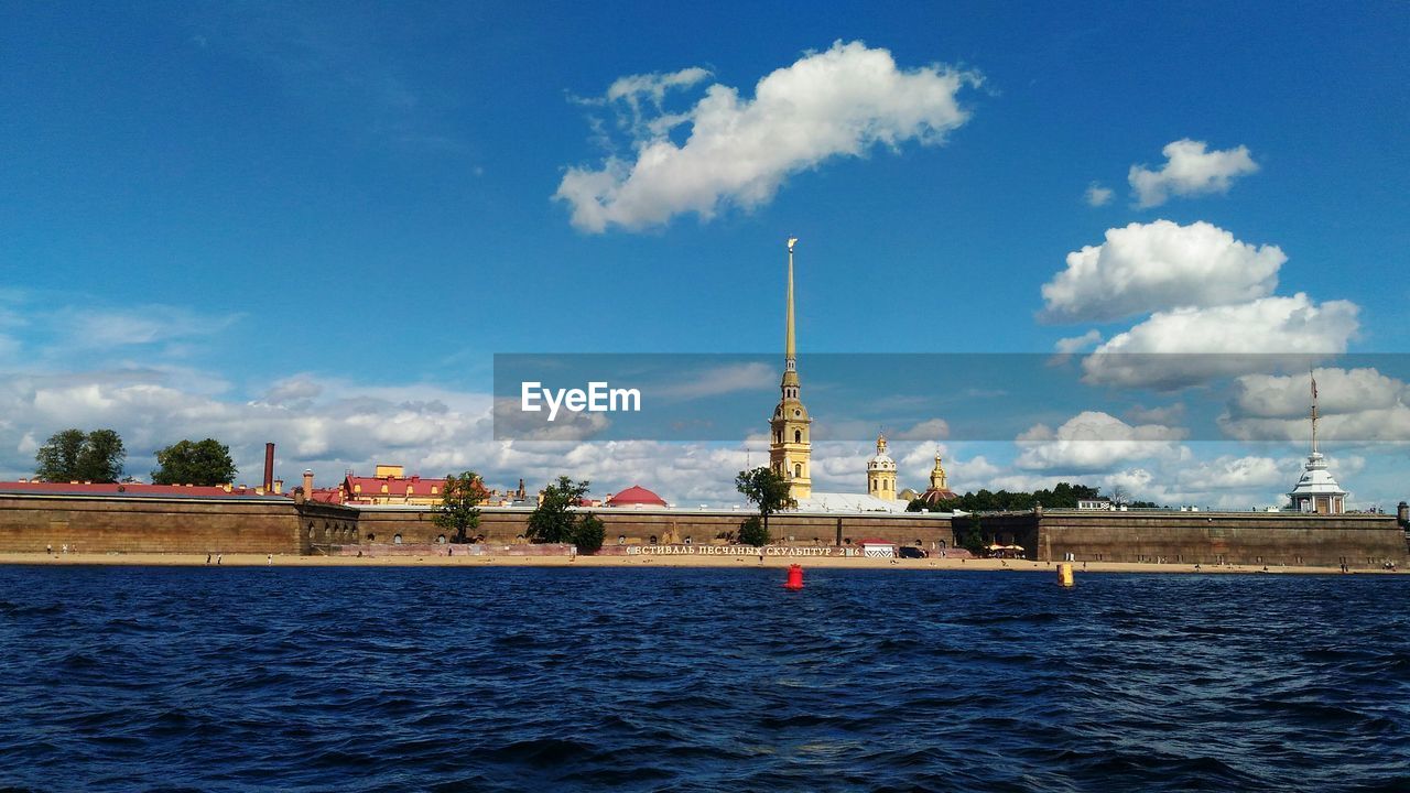 View of city at waterfront against cloudy sky