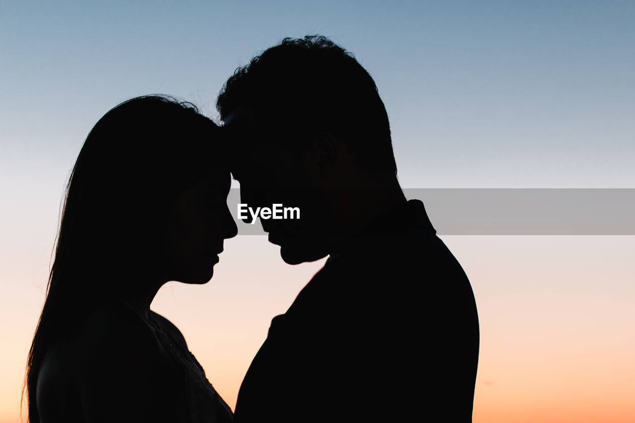 Close-up of silhouette couple embracing against clear sky during sunset