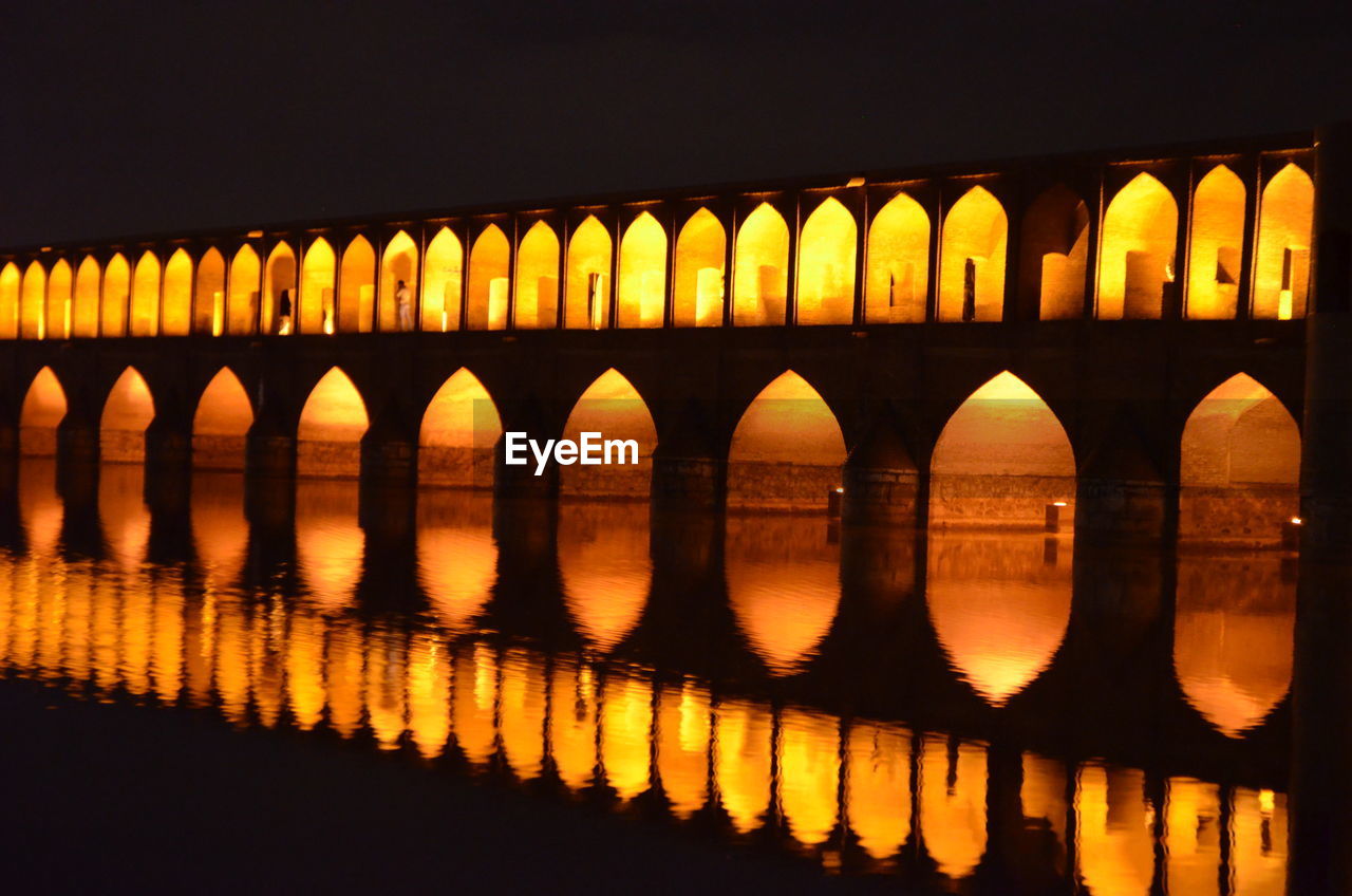 Illuminated arch bridge reflecting in river at night
