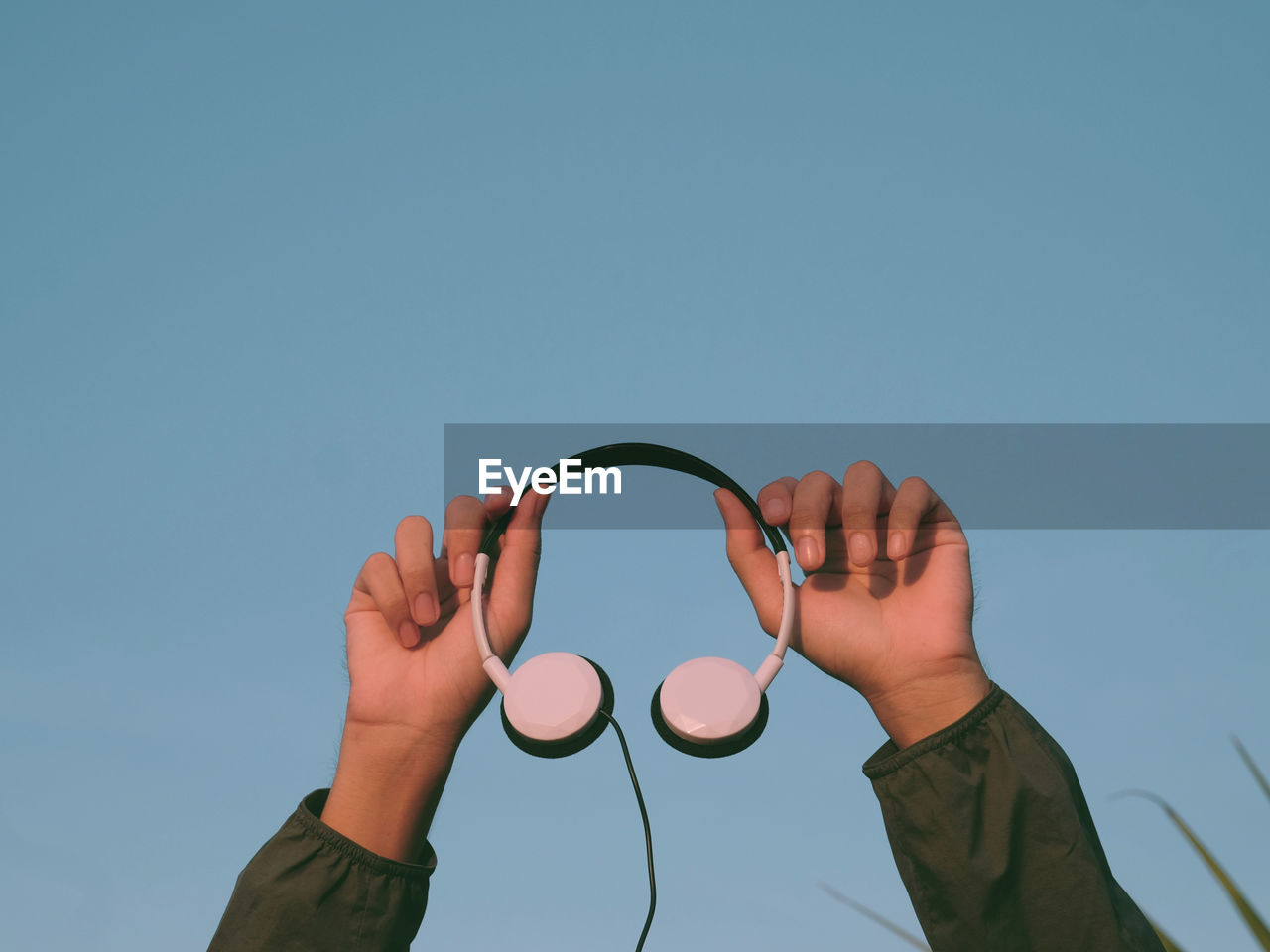 Low angle view of hand against blue sky , holding headphone