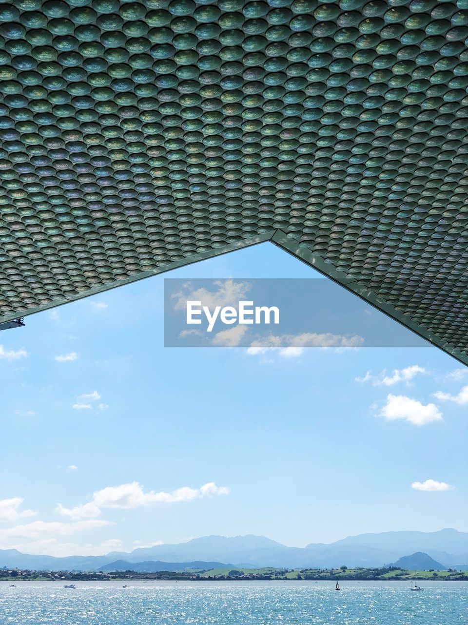 Low angle view of patterned ceiling by sea against blue sky