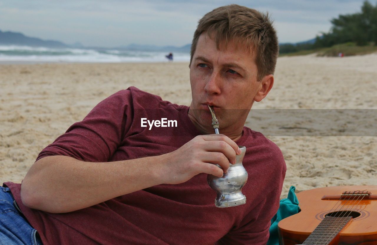 Young man drinking yerba mate while relaxing at sandy beach