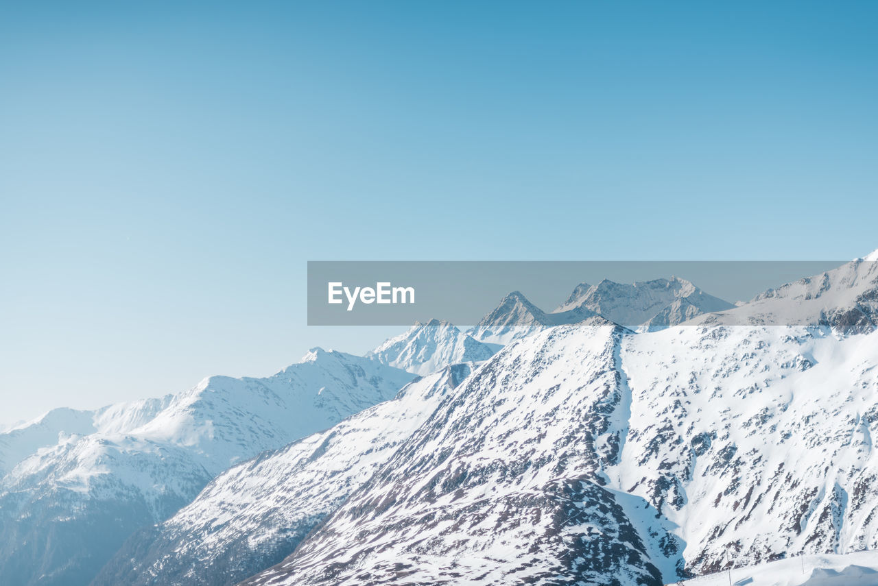 Scenic view of snow covered mountains against clear blue sky