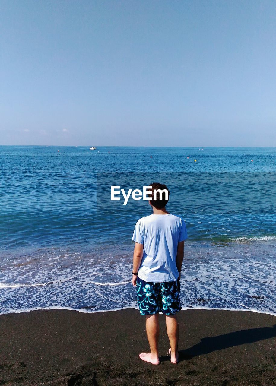 Rear view of man standing in front of sea