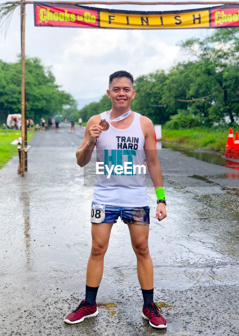 Portrait of athlete holding medal while standing on wet street