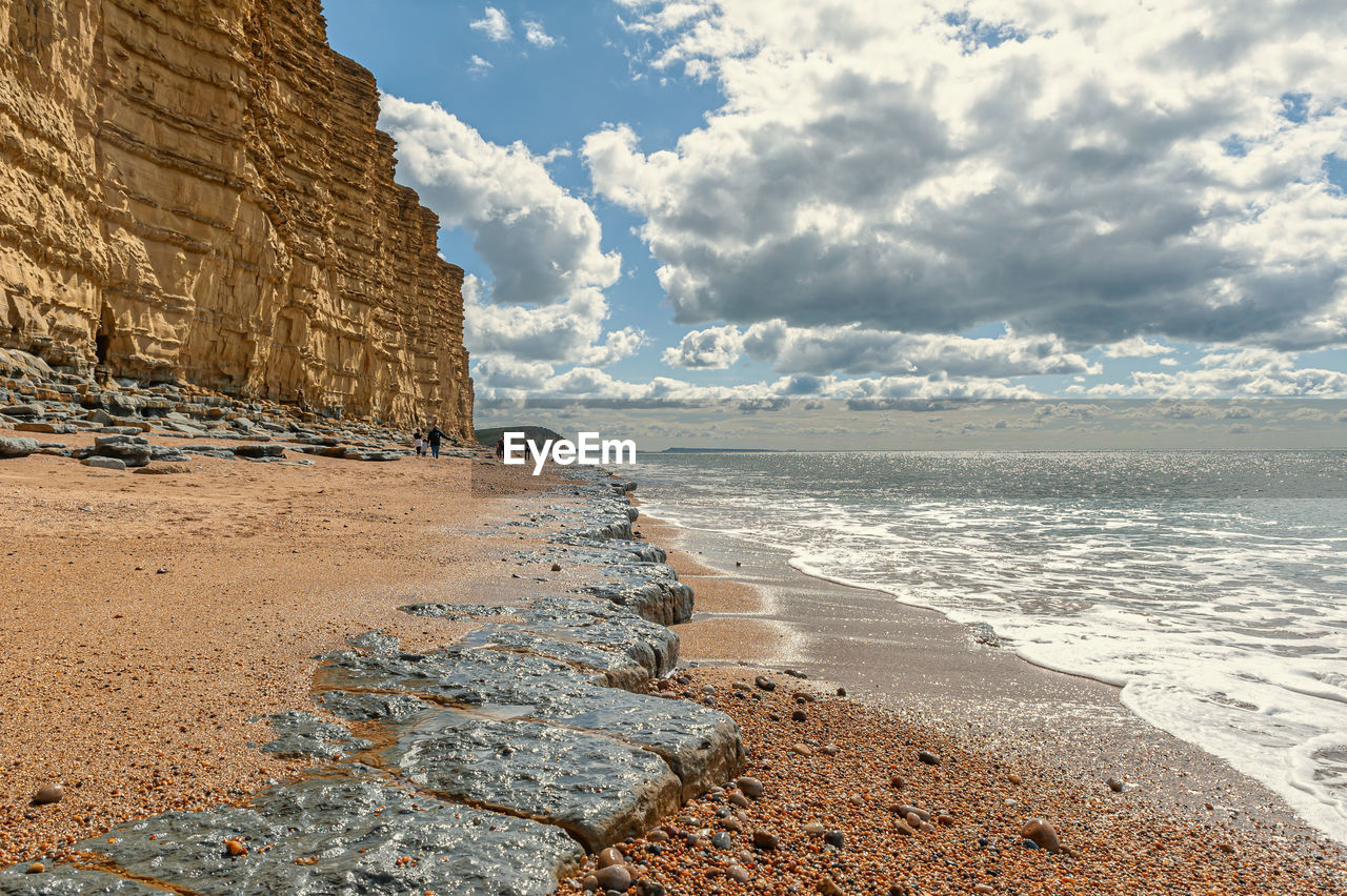 Distant view of mother and kids walking on beach by rock formation against sky
