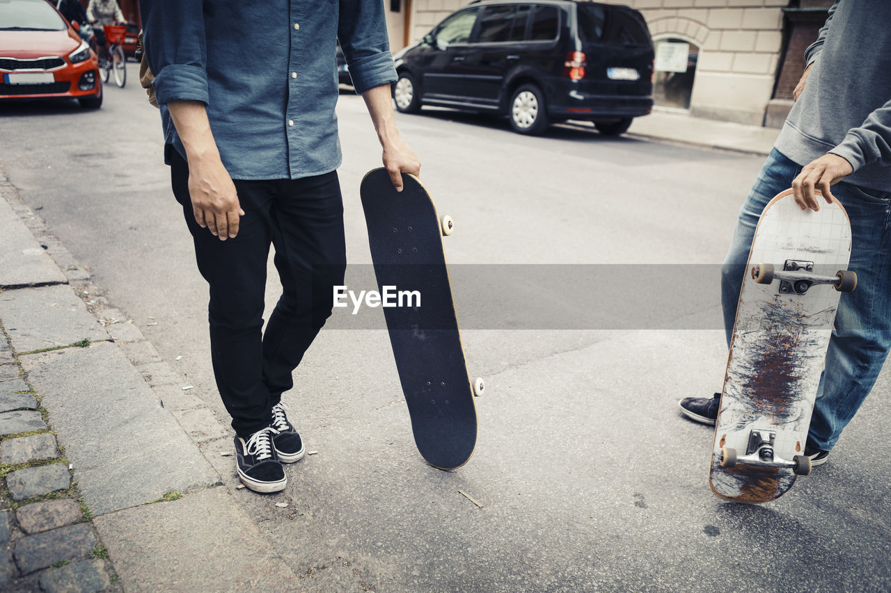 Low section of male friends with skateboard on street