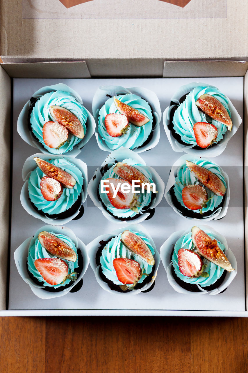 The plate of tasty cupcakes decorated with strawberry, fig and cream