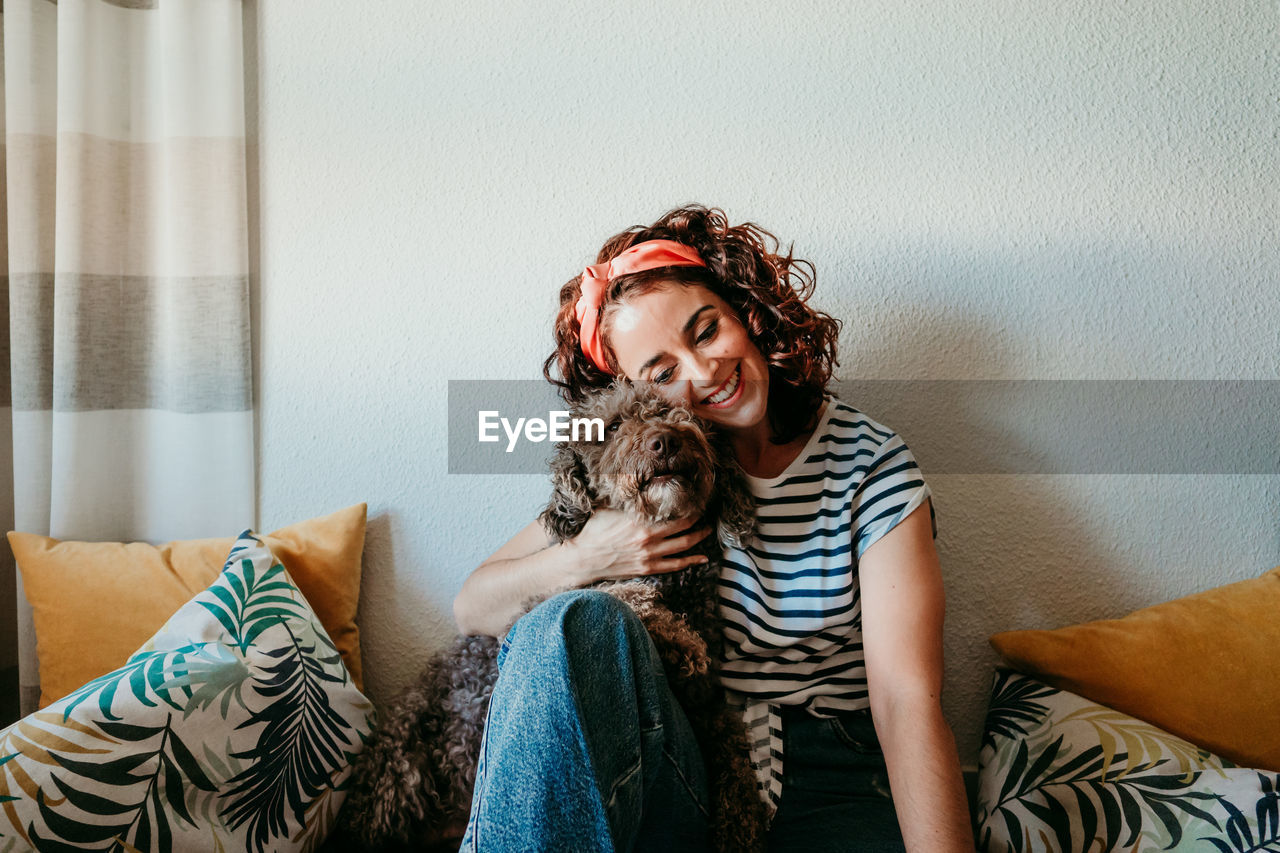 Woman embracing dog by wall at home