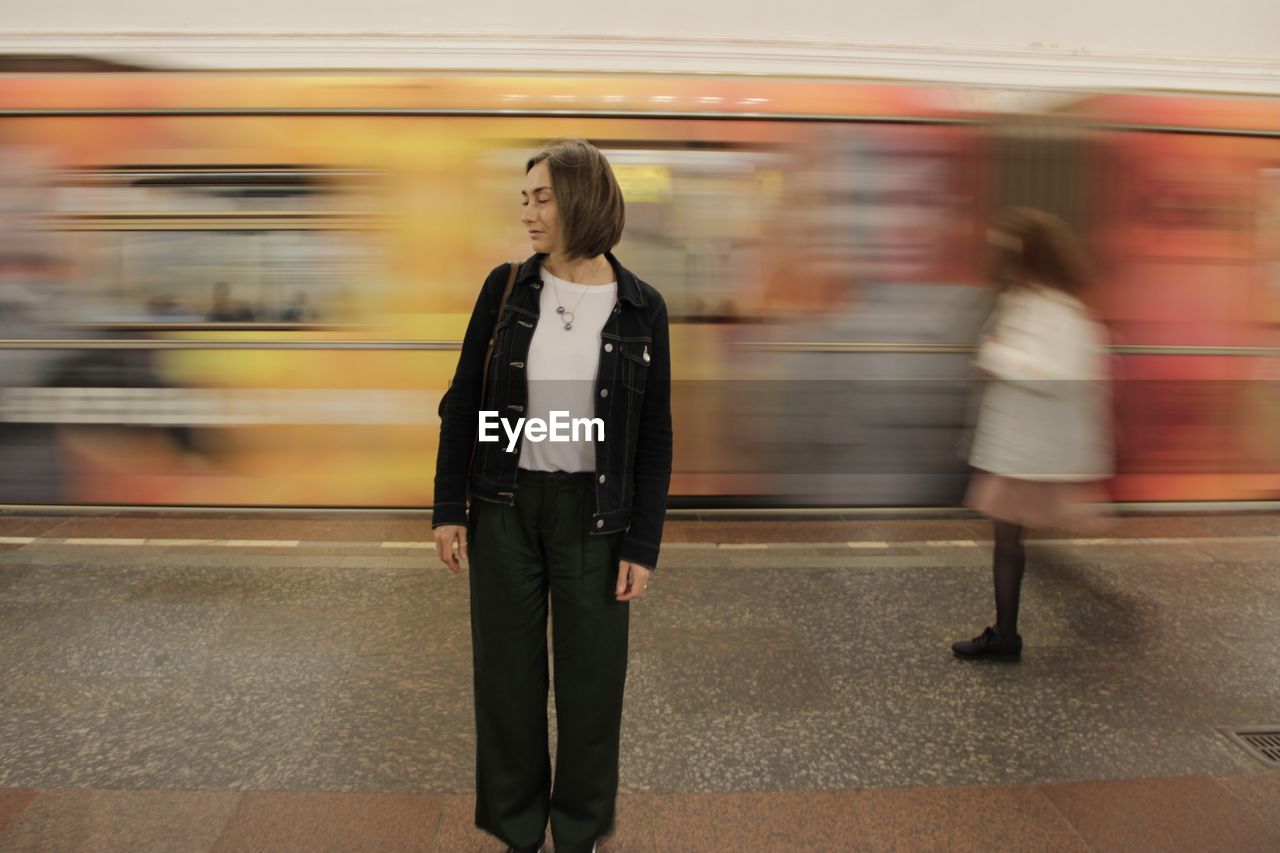 Blurred motion of train at railroad station and static girl