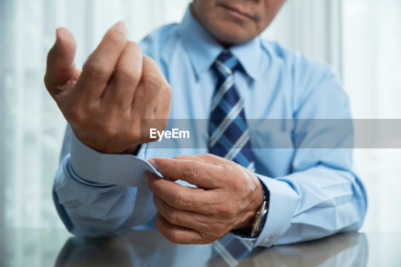 Midsection of businessman buttoning sleeve at desk