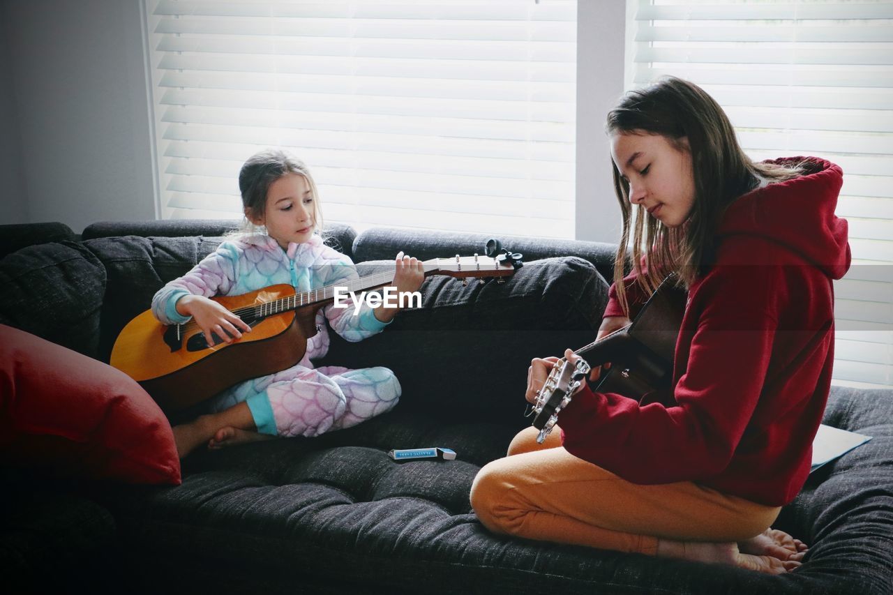Two little girls playing guitar sitting on sofa at home