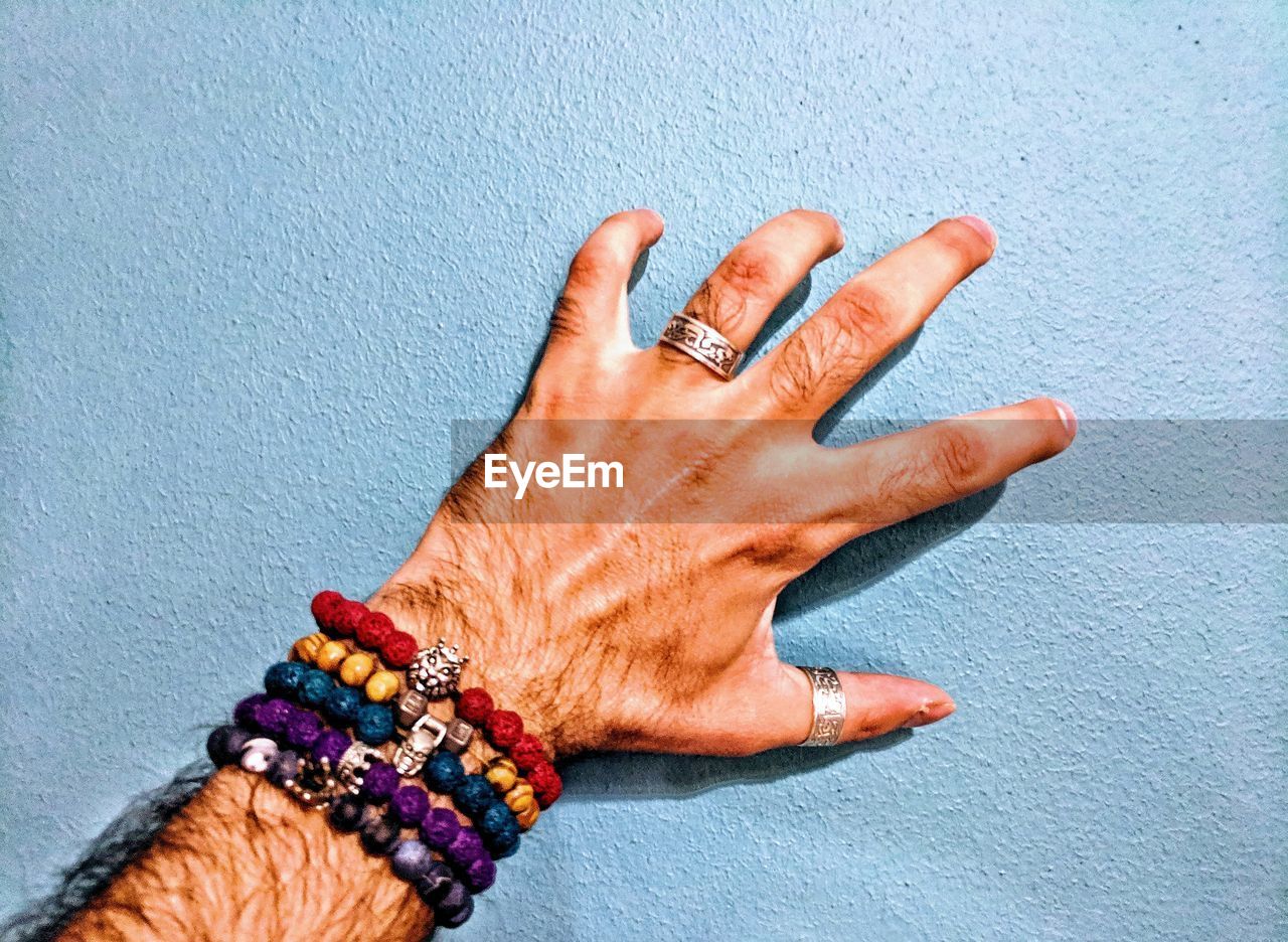 Cropped hand of man wearing bracelets touching on wall