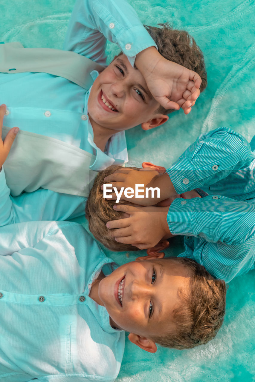High angle view of smiling brothers lying on bed
