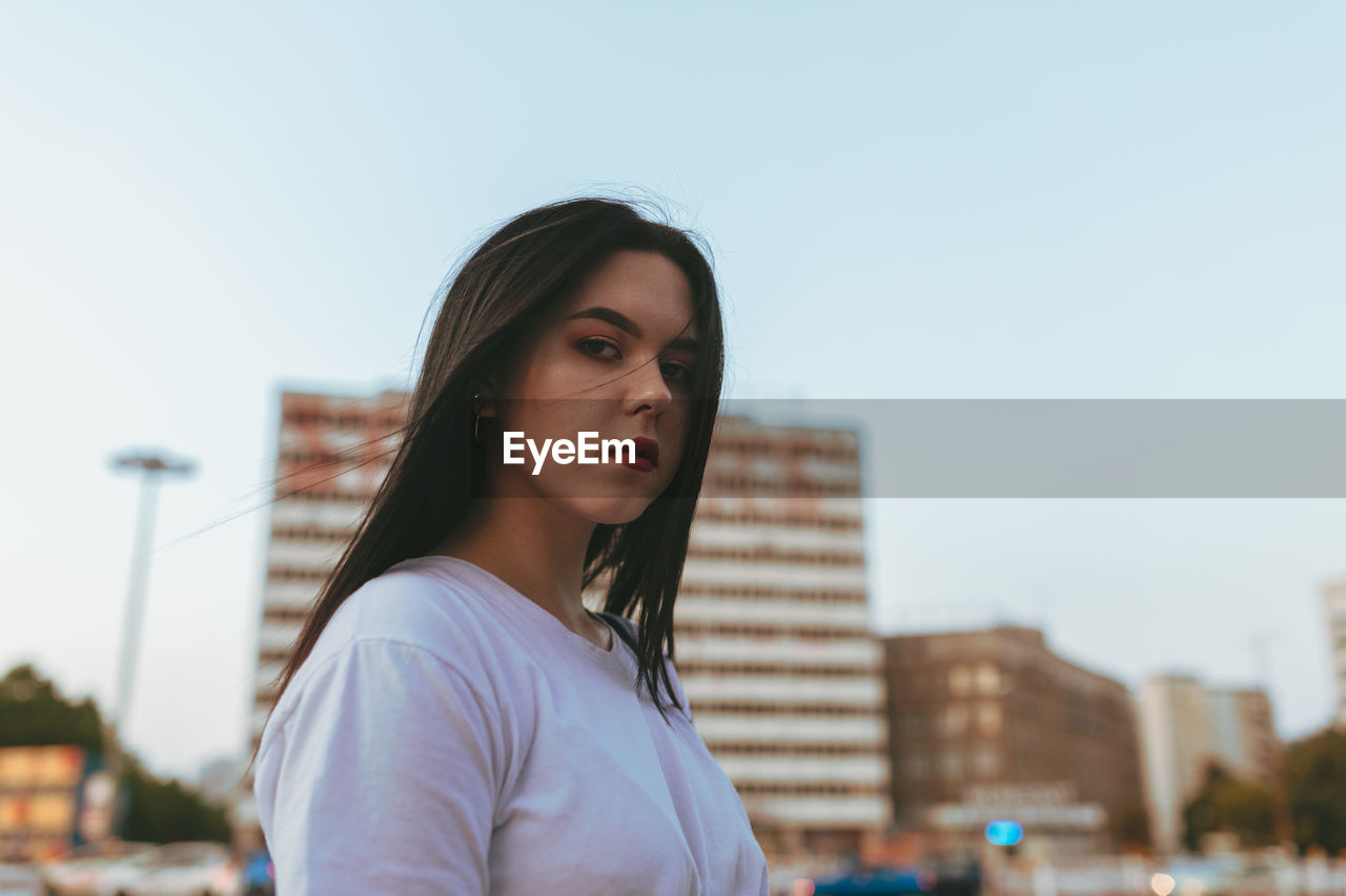 Low angle view portrait of young woman standing in city against sky